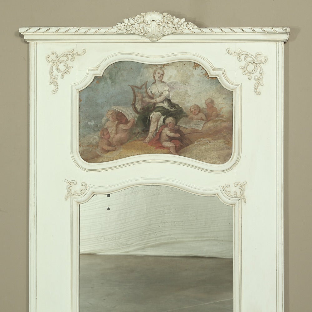 Boasting a patinated painted finish that has achieved a lovely patina, this 19th century country French trumeau features a classical romantic scene on the oil painting above, with a generous beveled mirror below, all surrounded by carved