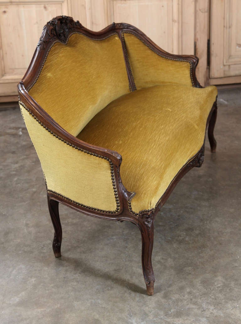 This gracious Antique 19th century French Walnut Louis XV  Lisette Settee exhibits great state of preservation with velvet atop hand carved French walnut elegant rococo frame with curved back, scrolled arms. Originally a part of French boudoir salon