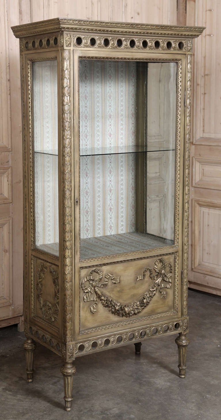 Hand-crafted antique furniture from fine Italian walnut was given a painted gilt finish that has achieved a quaint distressed patina over the decades, this elegant vitrine glazed front door and sides for ideal display. Spiral ribbon, laurel garland,