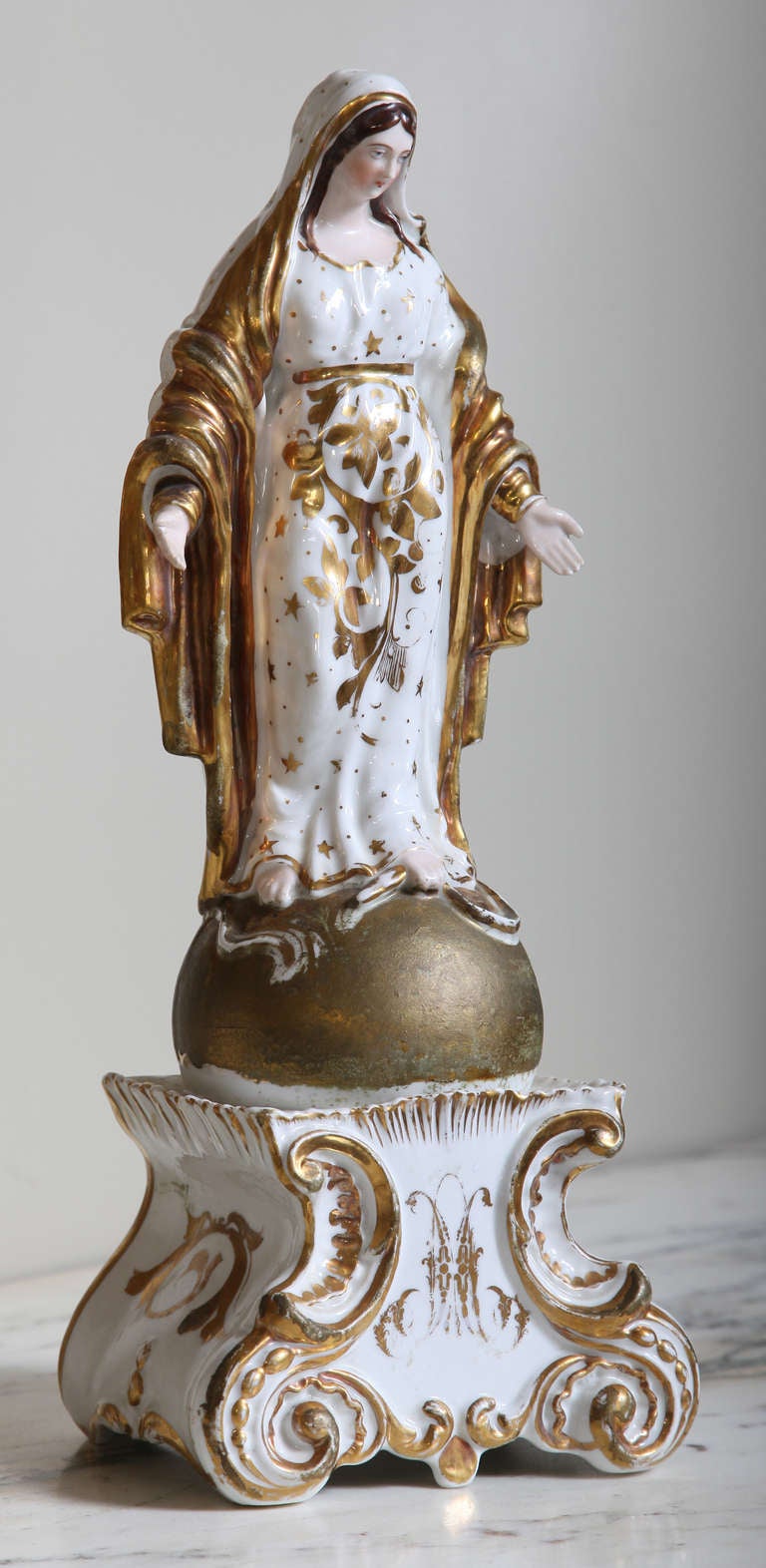 Cast in fine white porcelain, then lovingly hand-painted and accented with gold, then finally glazed and fired to preserve its beauty, this depiction of Madonna on a pedestal is truly a work of the devotee's art.