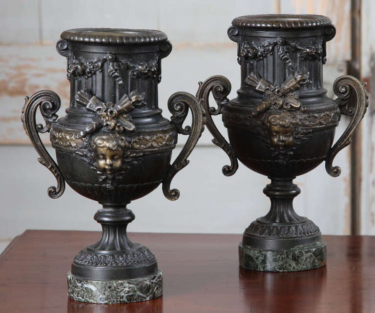Elegant spelter French Louis XVI style neoclassical urns given a two-toned patinaed finish, and set upon original marble bases, as they were crafted in 19th century. This charming pair of urns would typically bear flowers or fresh greenery to liven