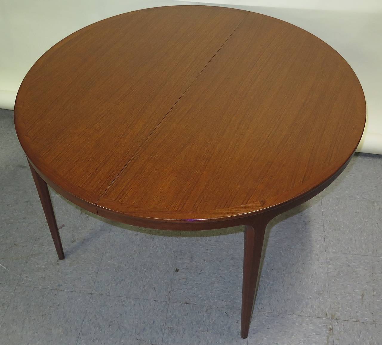 Restored. Teak. Nice leg design. Few scuffs and nicks under new surface. Without leaves measures 45.25 in. round x 28.25 in. high. Each leaf measures 21 5/8 in. W. When all four leaves are in a pair of legs in center drop down. Total of 130