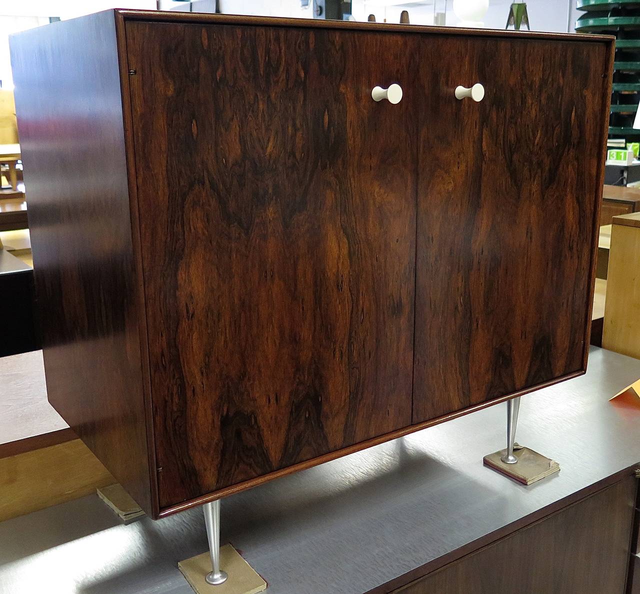 Beautiful two-door cabinet in rosewood with very active grain. Two Bakelite pulls. Aluminum legs. Inside there is one adjustable shelf. The piece has been totally restored. The original label is inside cabinet.
