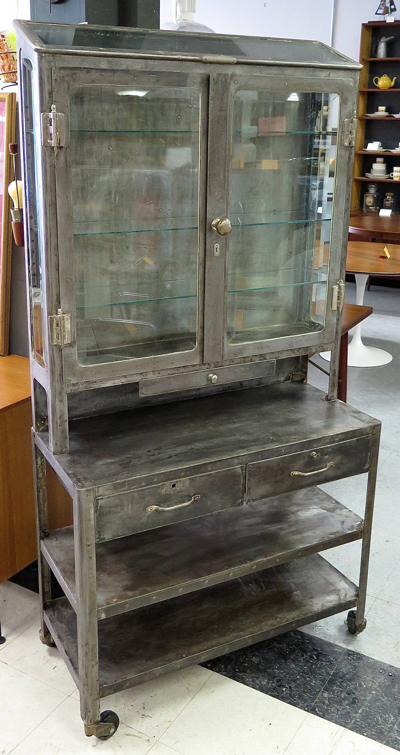 Made in Philadelphia. Steel construction. Nickel hinges and knobs.  All original beveled glass. 3 new glass shelves. New rubber wheels. Has some surface rust. Cabinet was all hand-scraped to its original finish. Great vintage piece!