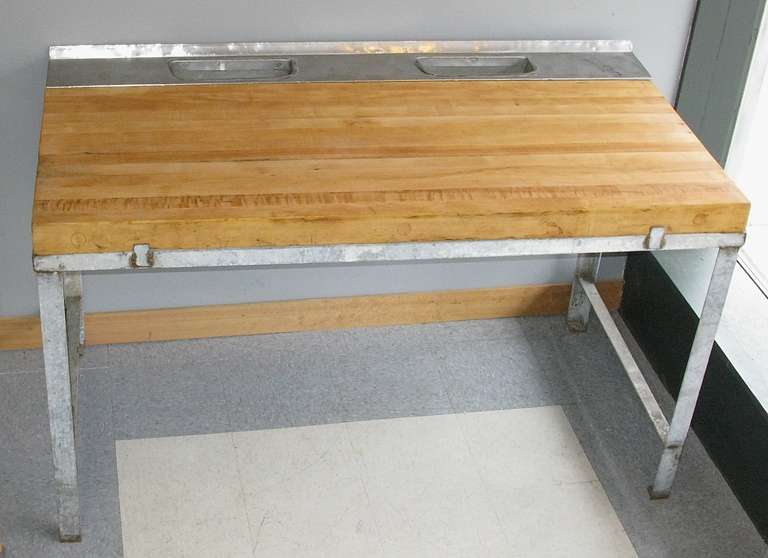 Vintage condition. Wood surface has been sanded and oiled. Base constructed of galvanized steel.  2 scrap chutes toward back of work area. Butcher block surface measures 24 inches deep, 60 inches long. Picture #5 is taken from underneath table to