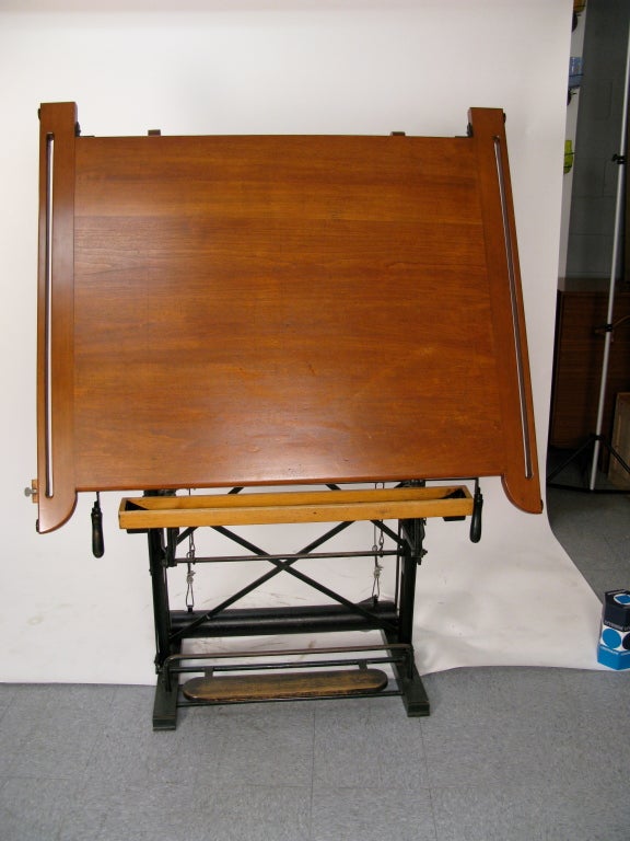 Cast iron base with wooden pedal to raise and lower table top. The table has it's original porcelain ink wells (2).The top goes completely flat to almost vertical.Two handles underneath the top are used to adjust the slope of the writing
