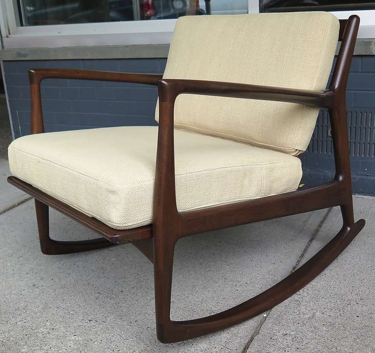 Refinished. Labeled. Dark teak. New upholstery in champagne. New straps. Some small marks on arm.