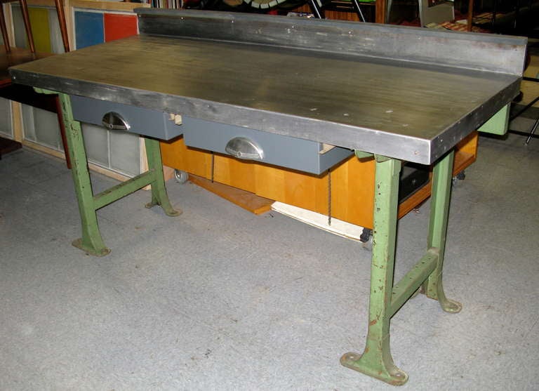 Original condition. Iron base supports. 2 metal drawers with stainless handles. Steel sheet top makes great work surface. Work area measures 34 inches high from floor. Top has 3 small filled holes on right. Extremely heavy!