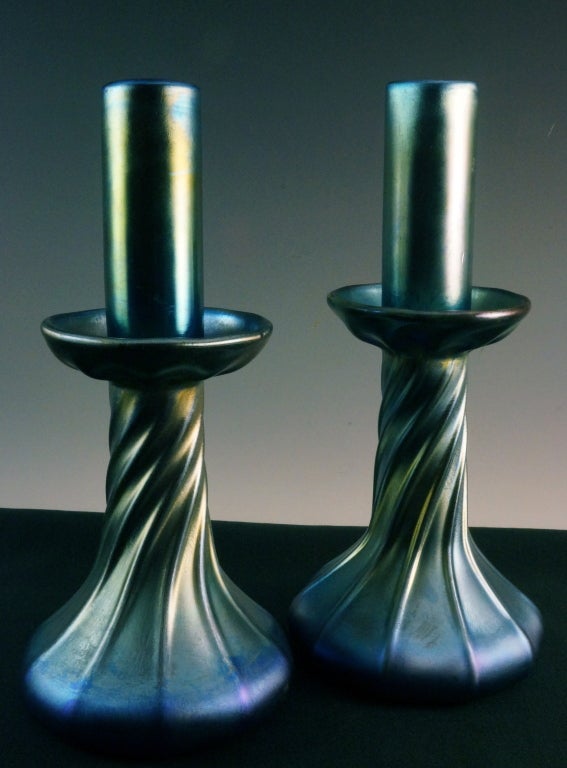 This is a pair of Tiffany candlesticks of blue favrile iridescent art glass. They are formed with a squat base and a spiral ribbed support. It is rare to find them with their fitter inserts as these have. There are Tiffany factory drilled holes in