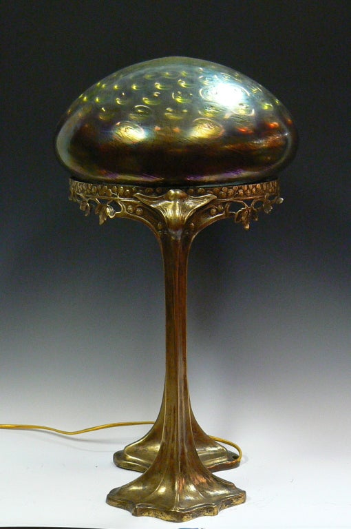 Bronze art nouveau base modeled as plant form supports an iridescent green art glass shade with bullseye decoration, probably Loetz. Very similar to the work of Gustav Gurschner, this was produced by Hermann Eichberg. The base was executed by