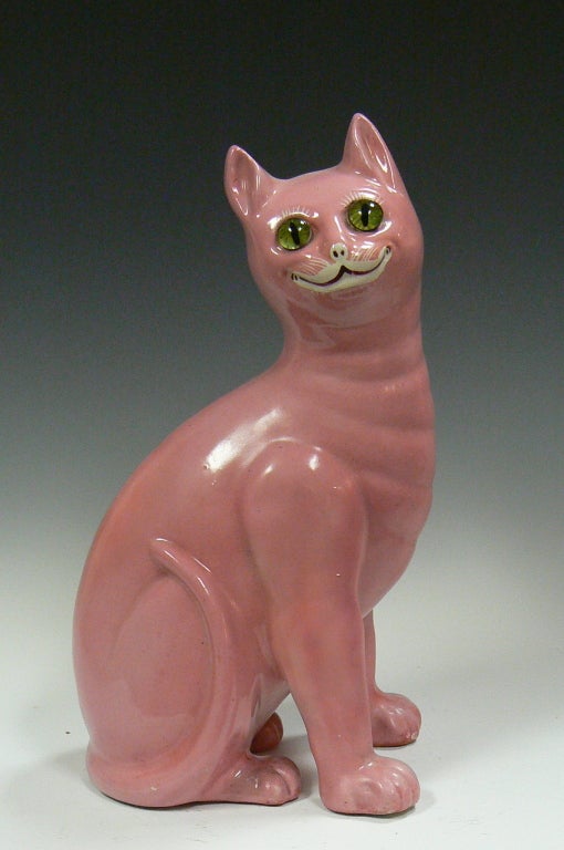 Grinning pink ceramic cat with green glass eyes, white eyelashes and whiskers in the style of Galle. Dating to the 1940's this whimsical kitty was produced in the United Kingdom.