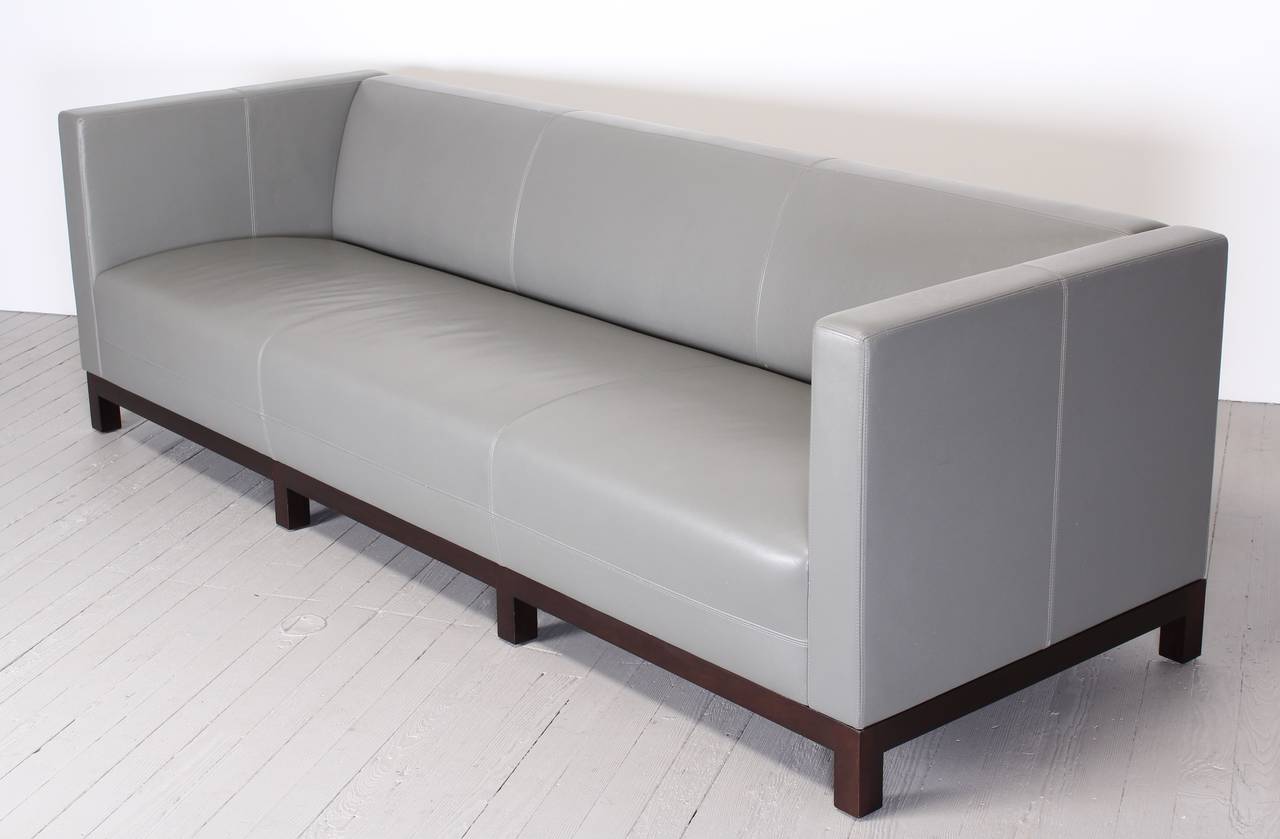 A Christian Liaigre sofa done in grey leather with saddle stitched design and mahogany base.