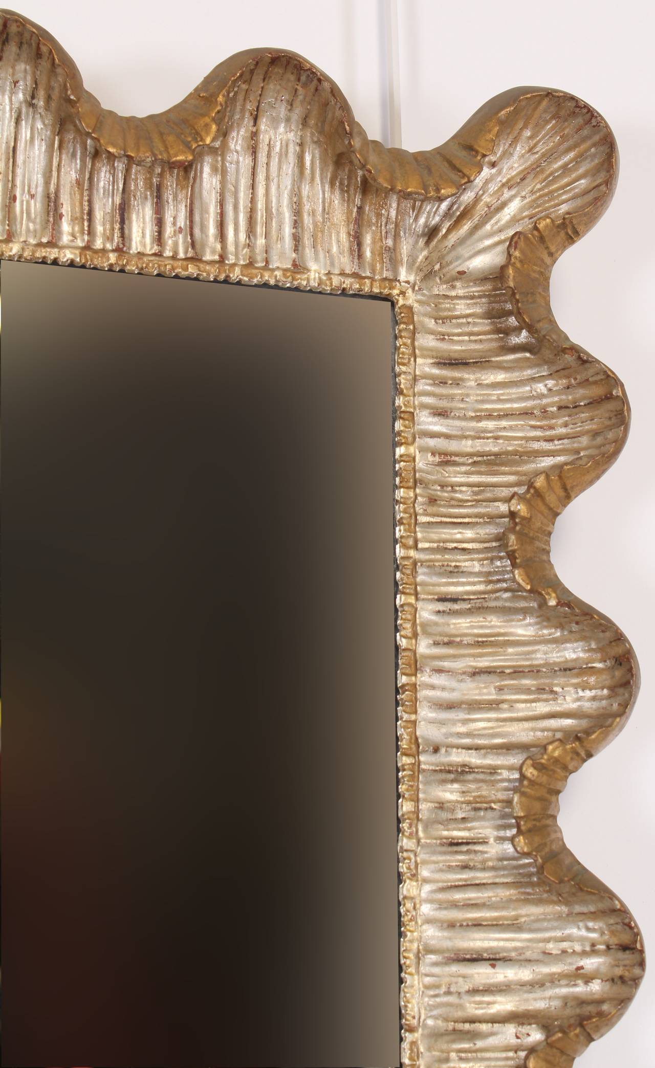 Wood carved, hand applied silver gilt with gold gilt background over gessoed frame, crafted in Italy during the 1950s. Has mounts that facilitate hanging the mirror either vertical or horizontal.