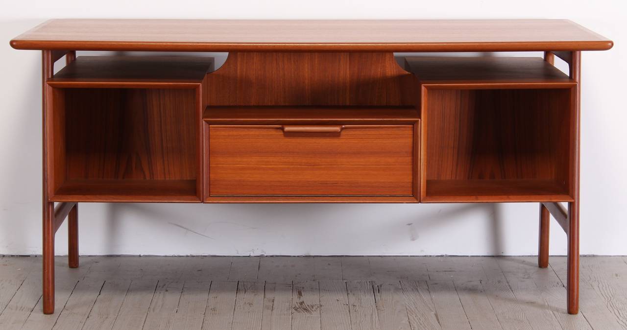 Exceptional Scandinavian teak desk designed by Gunni Omann for Omann Jun Møbelfabrik, model #75. 1960's. Floating modernist designed top with great angled sides, drop down door compartment on back of desk, and beautiful sculptural handles on