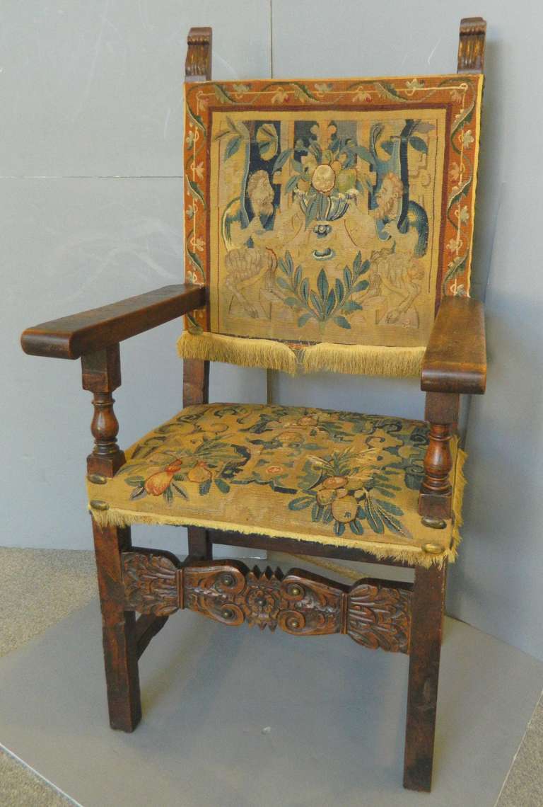 An 18th or 19th century antique Italian carved Renaissance style armchair.  The chair is upholstered with antique tapestry fragments with fringe on the bottom.