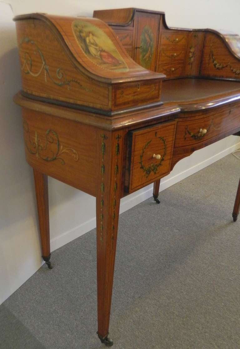 An early 20th century Sheraton revival satinwood, kingwood crossbanded, line inlaid and classical polychrome painted Carlton House style desk.
The curved superstructure is painted with a rose bouquet, portrait medallions, cherubs and floral