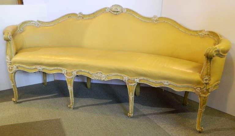 Antique Italian sofa with serpentine shaped back, roll upholstered arms, decorated with wreath and shells on the top rail. The wood frame has yellow and cream paint.  This late 18th century or early 19th century sofa has soft yellow leather