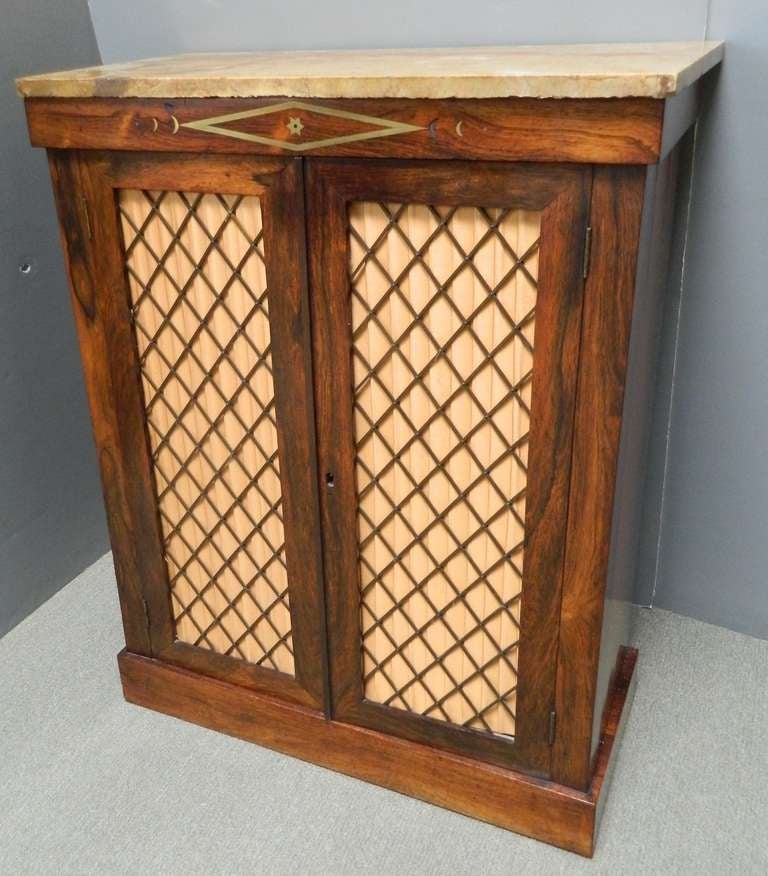 Pair of English highly figured veneer small side cabinets with brass regency diamond lattice grille and lift off marble tops. Each has  two grille work doors with interior shelves on plinth base and restrained brass inlay on the fronts..
These