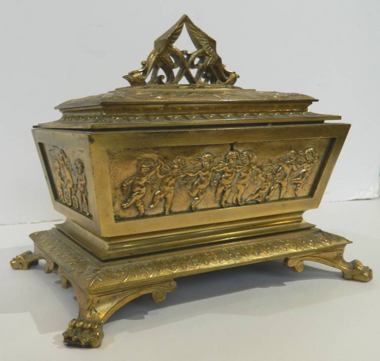 Antique 19th century polished bronze jewelry casket with paw feet and waterbirds finial. The sides have raised winged frolicking cherubs.