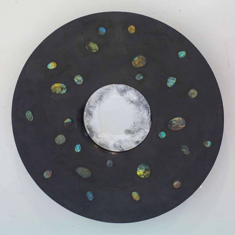 This mirror is created over a carved wooden form, with a hand applied polished black gesso surround into which 26 irridescent Labradorite stones are inset. At the centre is a 30cm diameter hand silvered convex mirror.
 
The Labradorite stones have