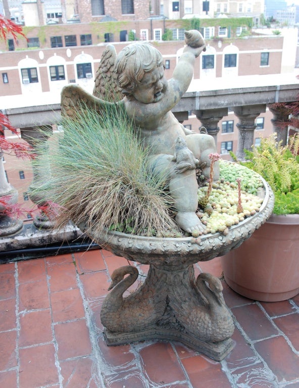 The winged putto is holding up a conch shell as if to strike the frog on his knee spitting water into his eyes, and is seated in a round basin supported by swans.  The overall modeling of the detail is superb.