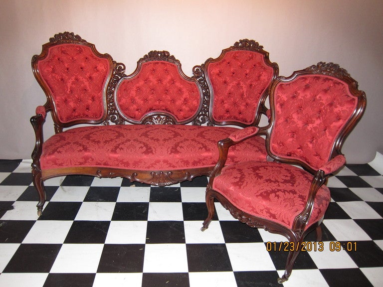 A most elaborate and ornate Rosewood Rococo Revival pierce carved floral parlor set. Consisting of a triple back sofa and matching armchair. Heavily carved with several different flowers & pierced leaf & scroll work in the center, raised on Cabriole