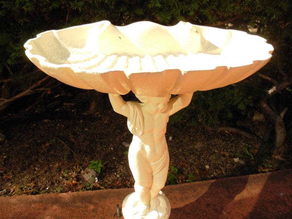 A 19th century cast iron birdbath, with a figural column of a cherub holding up a shell, has just been sandblasted and painted in a cream color.