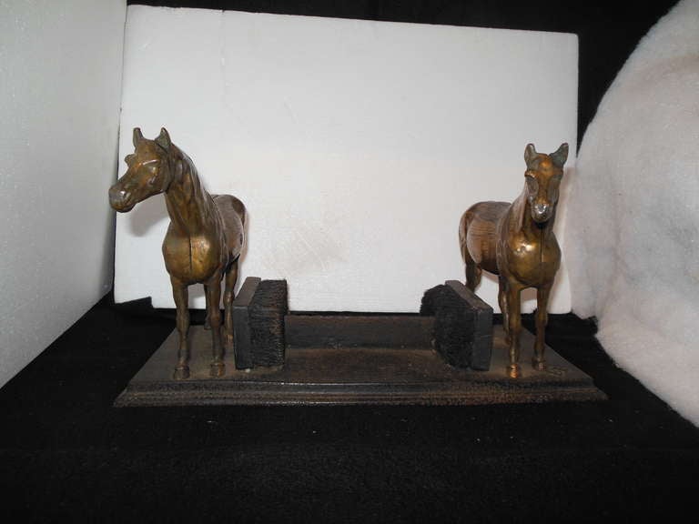 A cast iron base boot scraper, with two horses. The base is signed by the maker B. Butt, Baltimore. With two original brushes in good condition. The horses have a brass finish over the metal which exhibits some wear.