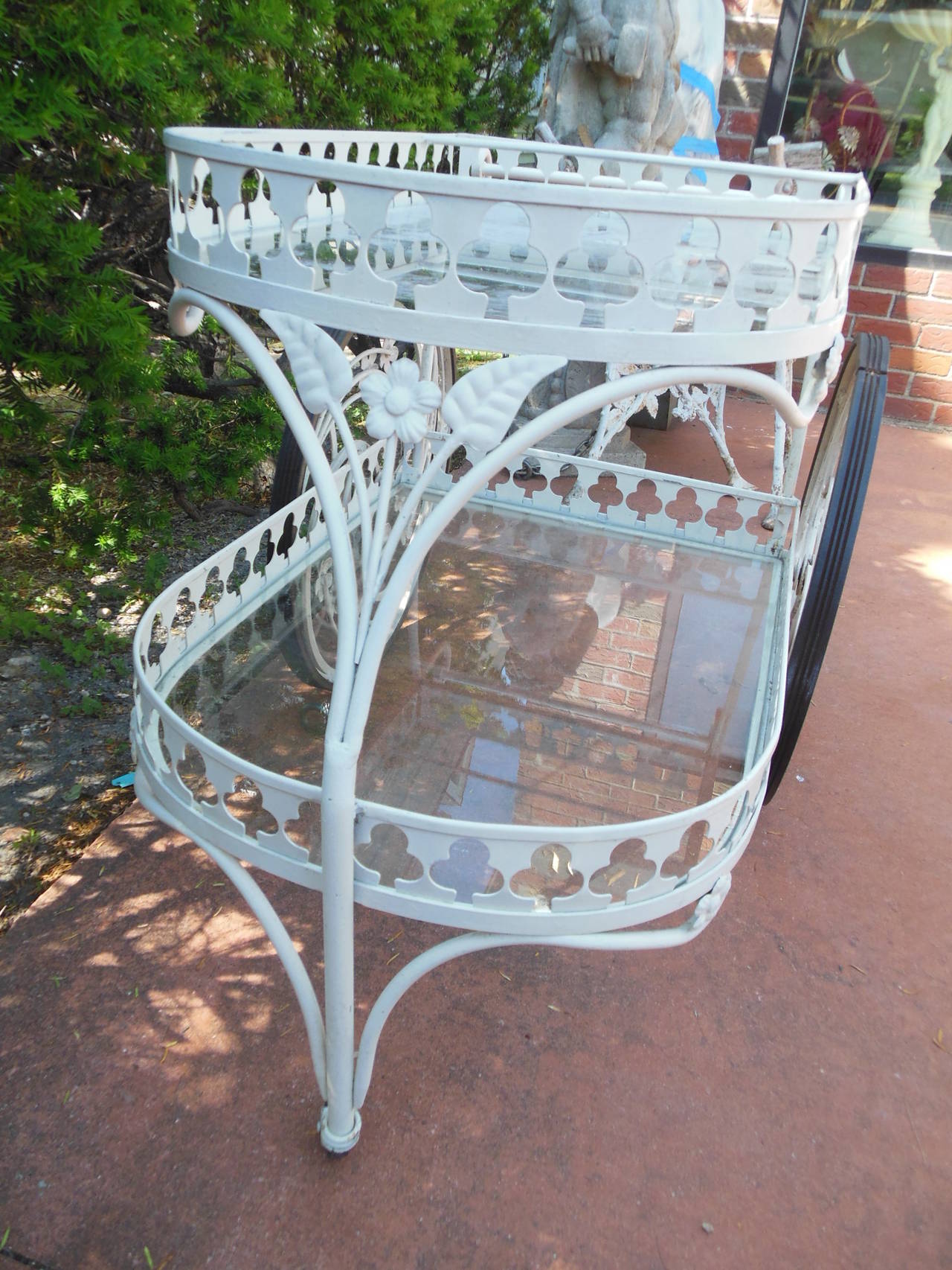 A most elaborate wrought iron tea cart by Salterini. With a huge wheel decorated with banana leaves and flowers. The apron with a border of three leaf clovers. The tea cart maintains its original factory finish. Unfortunately, the top piece of glass