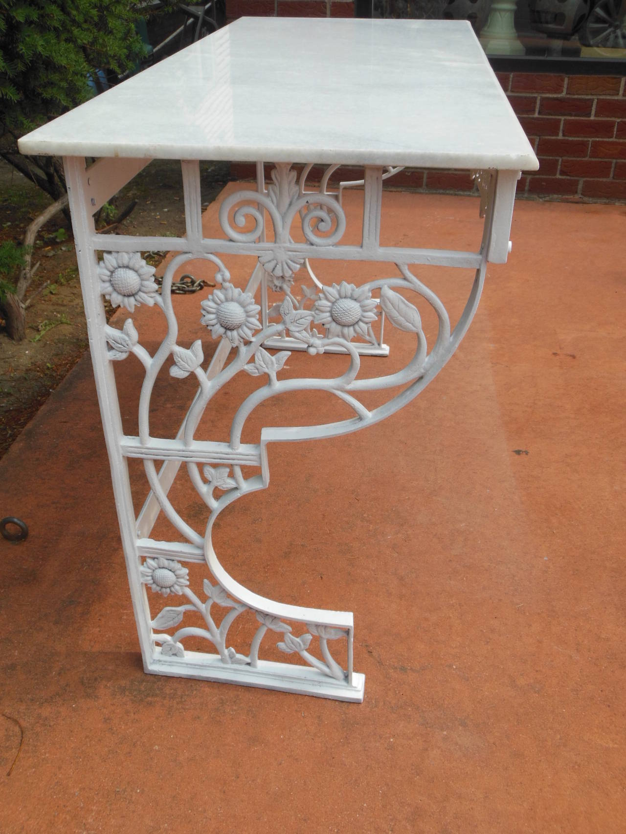 This is a marble-top cast iron console table in the aesthetic taste. The apron of the table is ablaze with pierce carved sunflower and pomegranate detail. The sides of the table decorated with more sunflowers.