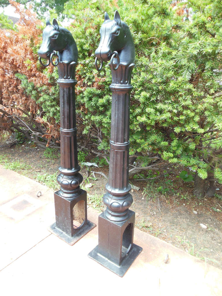 A pair of antique cast iron hitching posts, with horse heads and double rings on both. The posts have just been painted black.