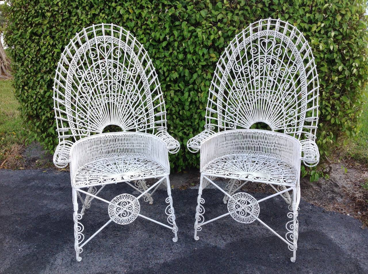 A pair of unusual fanciful iron wirework chairs with arched tops and barrel
Shaped backs. Ornate filigree designs end in rolled arms with lacy patterned
Seats. There are 