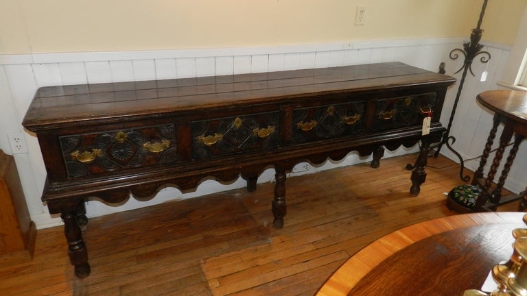 This is an early Scottish oak dresser with superb patina.  With an overhanging top above four heavily carved drawers, this piece exudes quality.  Fully dovetailed , each drawer has a  bottom of solid oak.  Solid brass handles and escutcheon plates