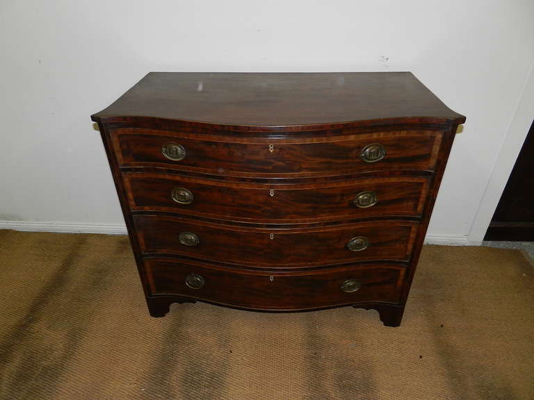 Mahogany inlaid serpentine fronted chest. The serpentine crossbanded, dovetailed drawers have brass oval handles. The sides of the chest are also shaped. This piece has inlaid canted corners and is supported upon the original bracket feet.