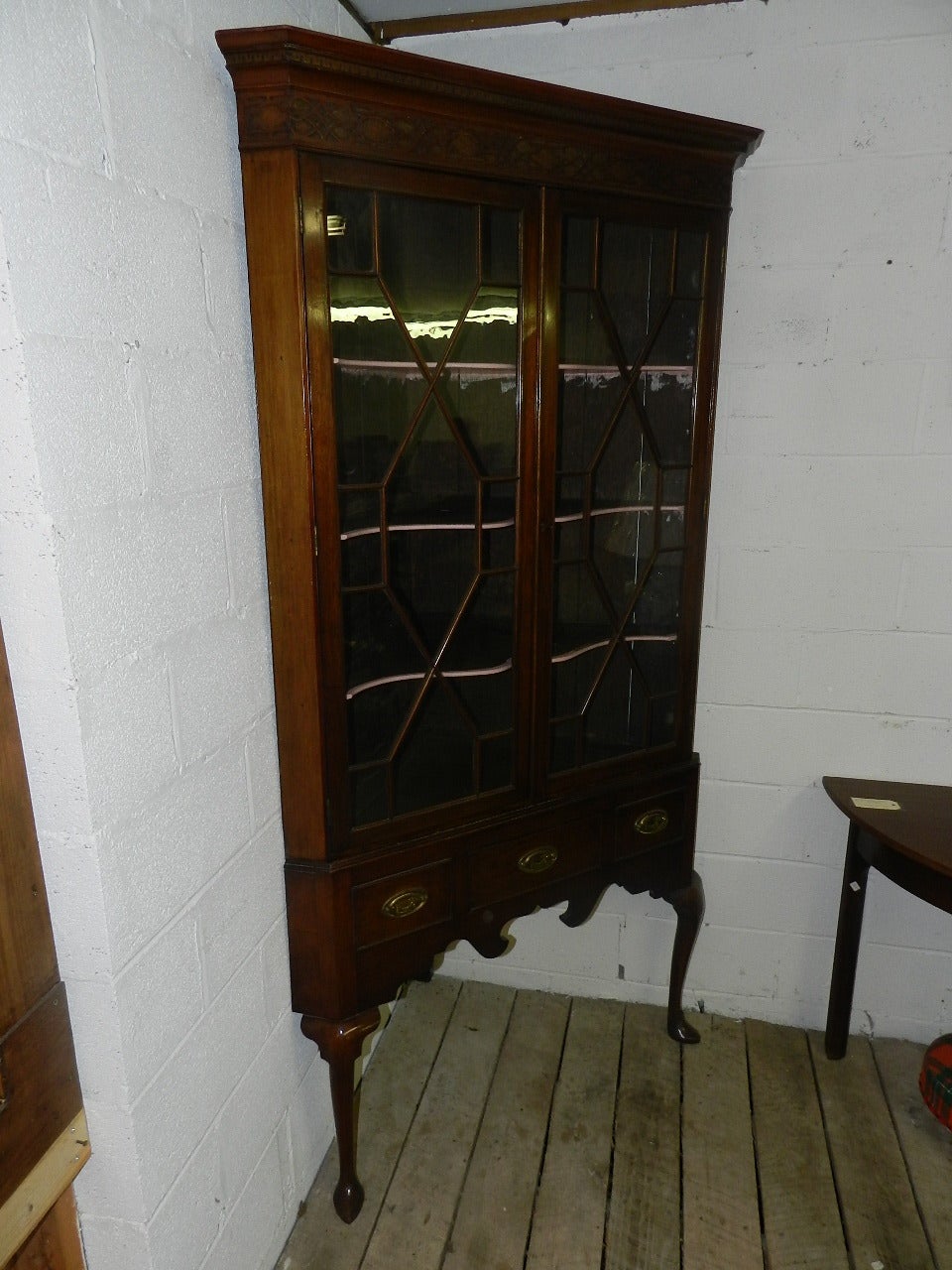 Mahogany corner cupboard .The upper section has a pair of 13 pane astragal glazed doors enclosing serpentine shaped shelves. The exterior has Chinese Chippendale style relief carving on the upper frieze. The lower section has a single opening drawer