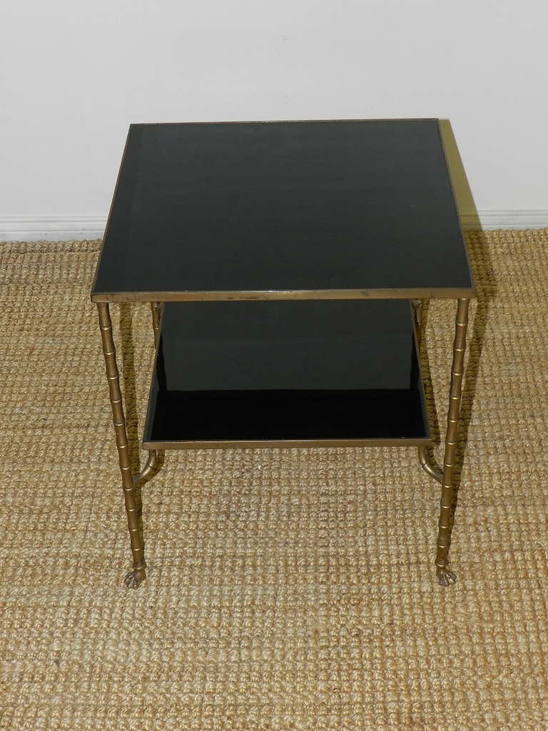 Designer end table with bronze effect faux bamboo legs terminating in paw feet. Inset in the table are two black glass shelves.
