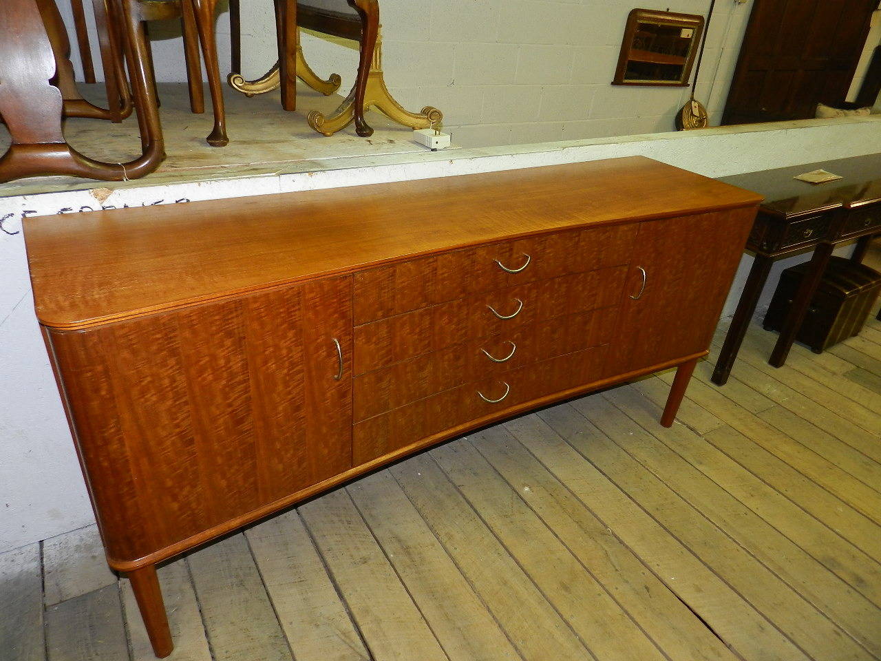 Mid-Century concave fronted sideboard in teak and Indian laurel. This streamlined server was designed by W. H. Russell F.S.I.A (Design R810), hand made by C. E. Grantham of Gordon Russell Ltd, Broadway, Worcester, England. (See image provided of