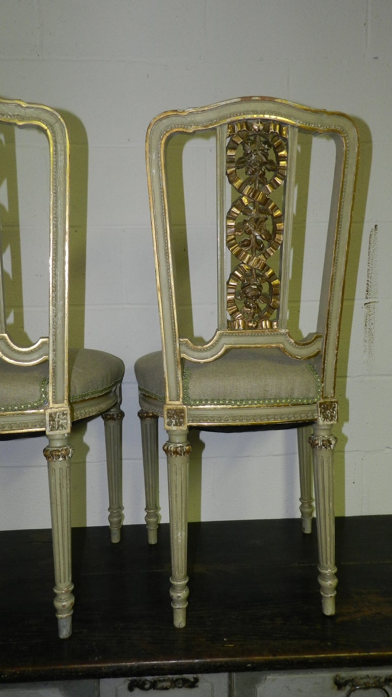  This is a lovely pair of gilt and french gray antique chairs with reeded legs and gilded shaped backs, The chairs are embellished with further decoration of gilded wooden faux ribbons encircling foliage to center of chair backs.  Covered in a