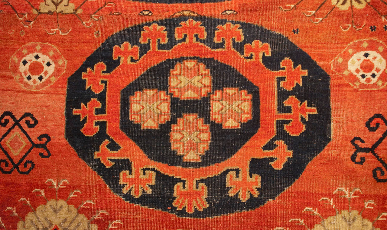 A late 19th century Central Asian Khotan rug with three large central medallions with floral and cloud motifs, on a variegated crimson background, amidst a field of flowers, surrounded by a contrasting floral border.