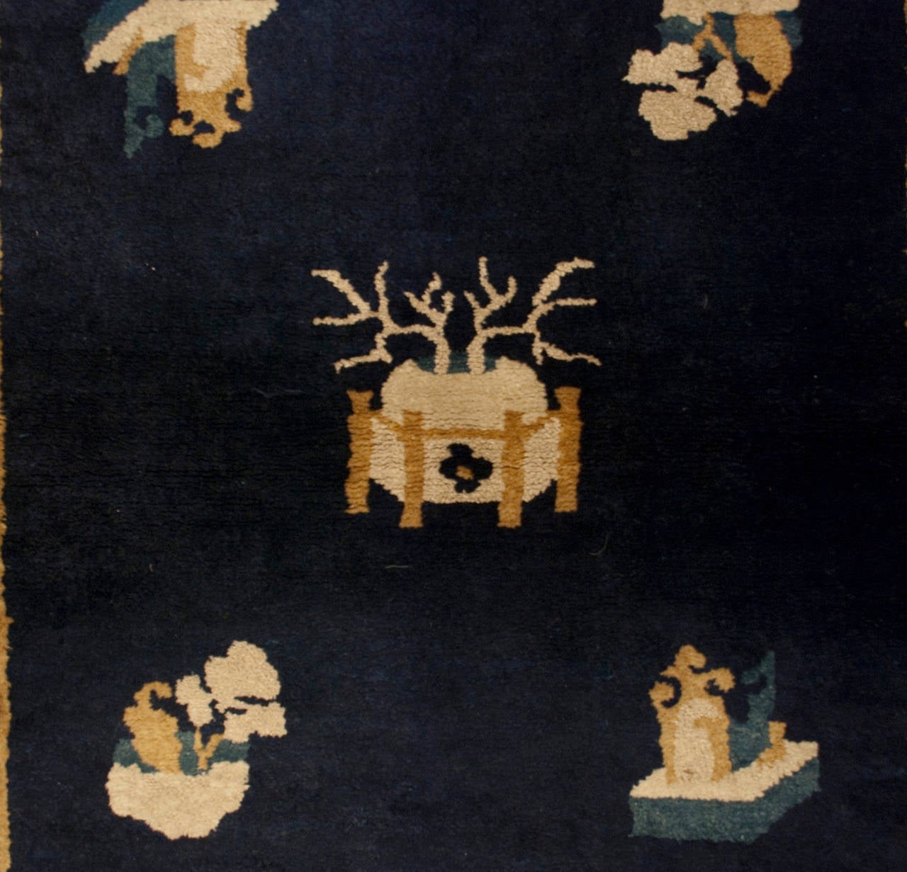An early 20th century Chinese Peking rug with scholar's objects amidst a beautiful indigo background, surrounded by a contrasting beige border with potted flowers and other scholar's objects.