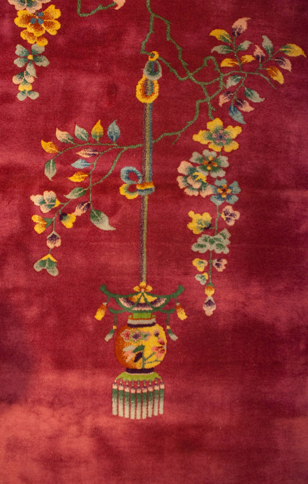 An early 20th century Chinese Art Deco rug with a brilliant borderless cranberry field and an asymmetrical motif of multicolored flowers, and a flowering tree branch with a hanging lantern.
