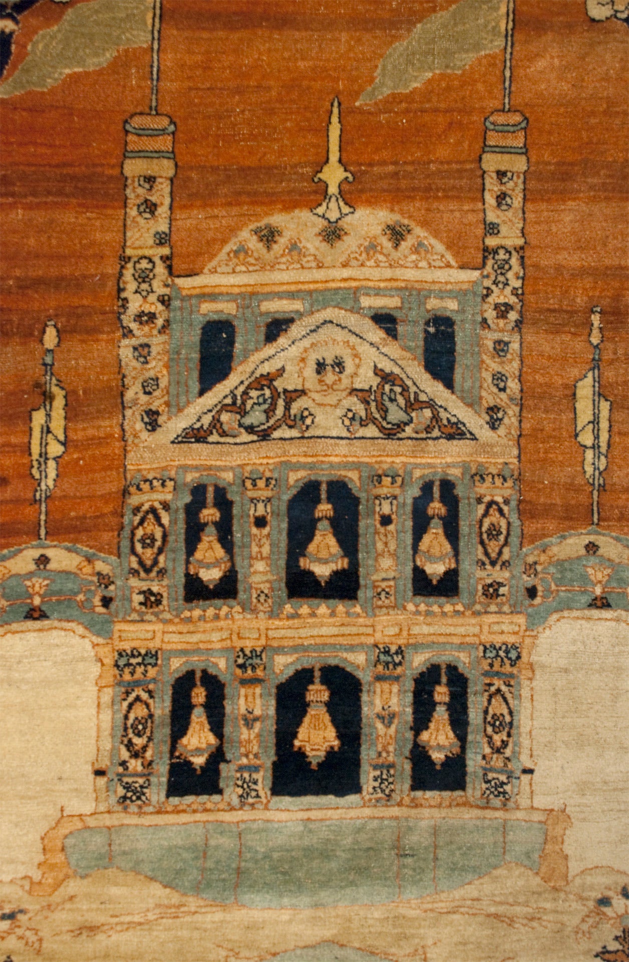 An amazing 19th century Persian Haji Jalili Tabriz pictorial prayer rug depicting a beautifully rendered pale blue mosque in front of a rust colored sky with a fish pond in the foreground, flanked by two columns with beastly figures and surrounded