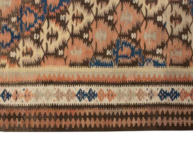 Un runner Qazvin Kilim persiano dell'inizio del XX secolo con un motivo geometrico a rombi incrociati multicolore circondato da bordi multipli a contrasto.
