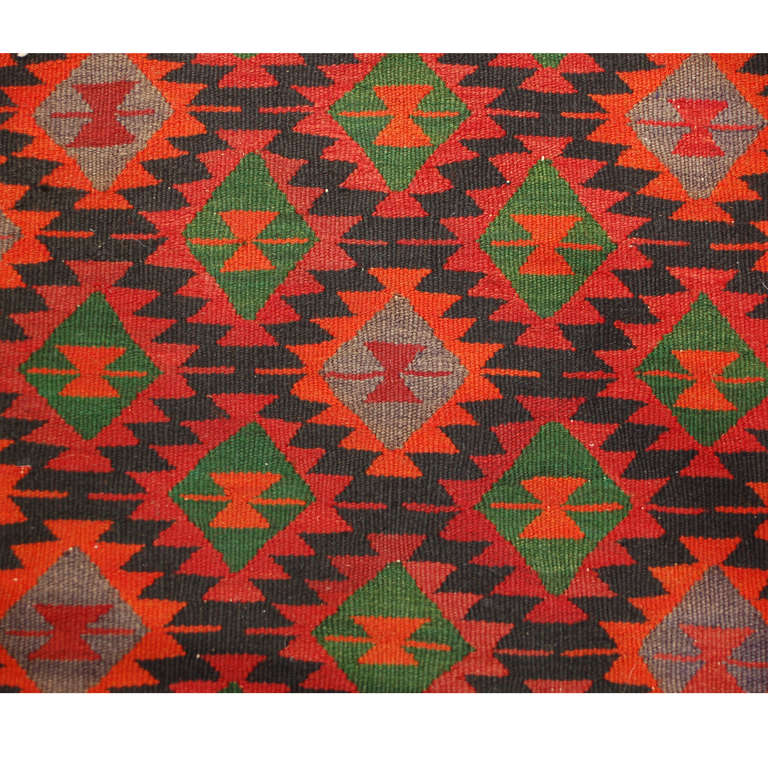 Ein Qazvin-Kilim-Läufer aus dem frühen 20. Jahrhundert (1930er Jahre) mit einem leuchtend karminroten, smaragdgrünen und orangefarbenen geometrischen Muster auf schwarzem Grund, umgeben von einer komplementären geometrischen Bordüre.
