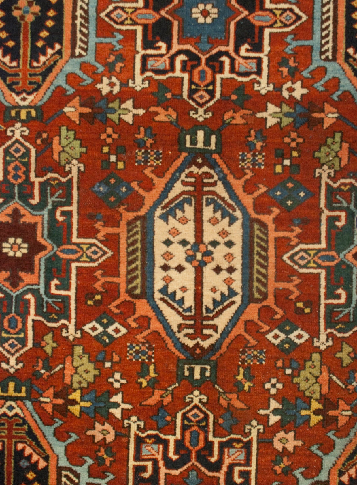 An early 20th century Persian Karaja Heriz rug with multiple large-scale geometric and floral medallions amidst a field of flowers, on a crimson background, surrounded by multiple floral borders.