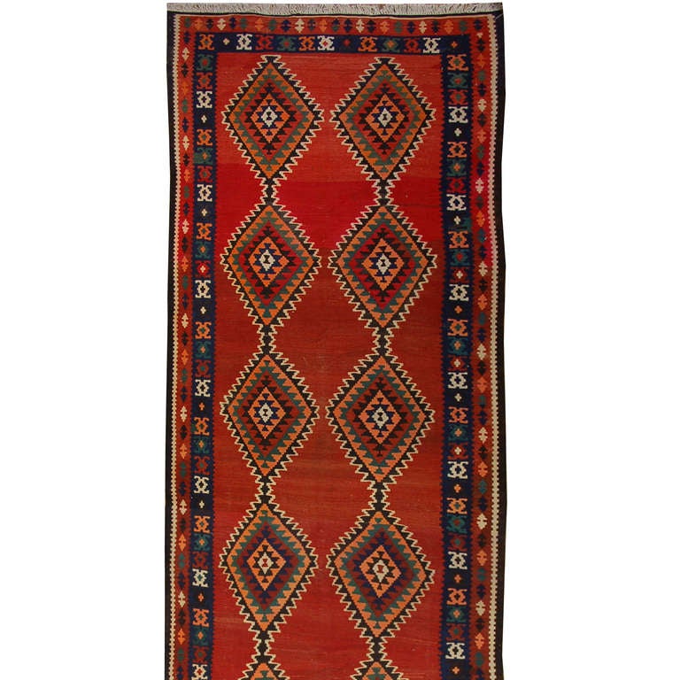 An early 20th century Persian Kilim runner with multiple multicolored diamond medallions on a variegated crimson background surrounded by a multicolored floral and geometric patterned border.