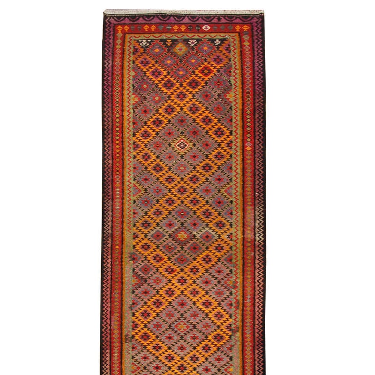An early 20th century Persian kilim runner with brilliant orange, crimson, and violet criss-crossing geometric pattern surrounded by multiple contrasting geometric borders.
