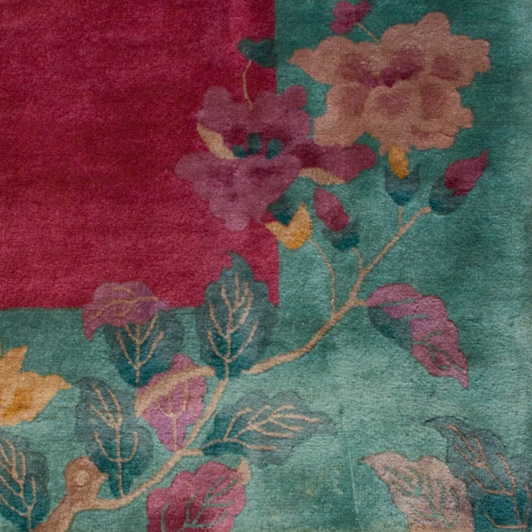 A Chinese Art Deco carpet with large multicolored floral branches on a cranberry field surrounded by a brilliant green border. Measures: 8'9