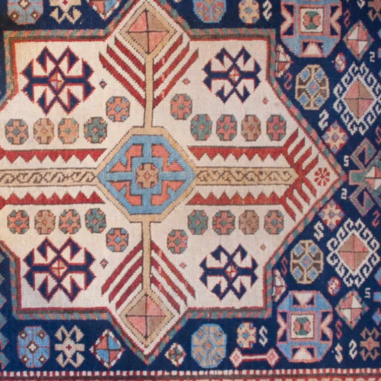 A 19th century Persian Kazak carpet runner with three central medallions surrounded by a field of densely woven tribal motifs, with a contrasting border. Measure:10'10