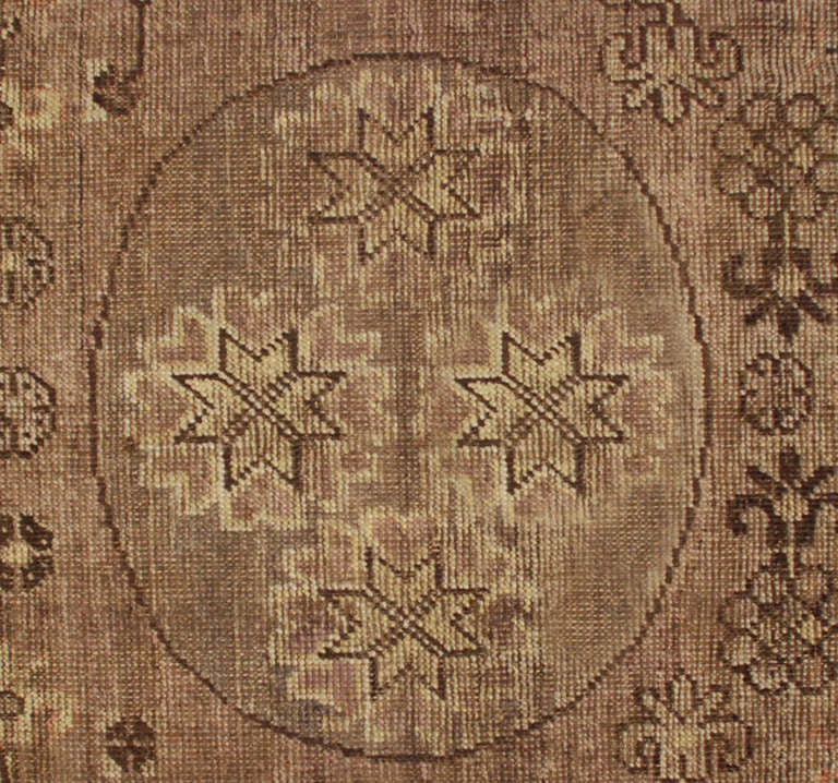 An antique Central Asian Khotan carpet with three large circular medallions on a dark lavender background, amidst multiple floral and geometric designs.

Measures: 3'4